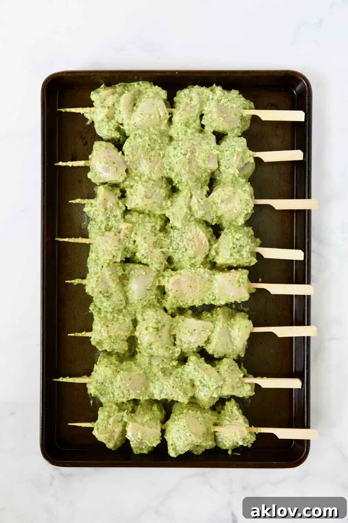Eight uncooked chicken skewers on rimmed sheet pan.