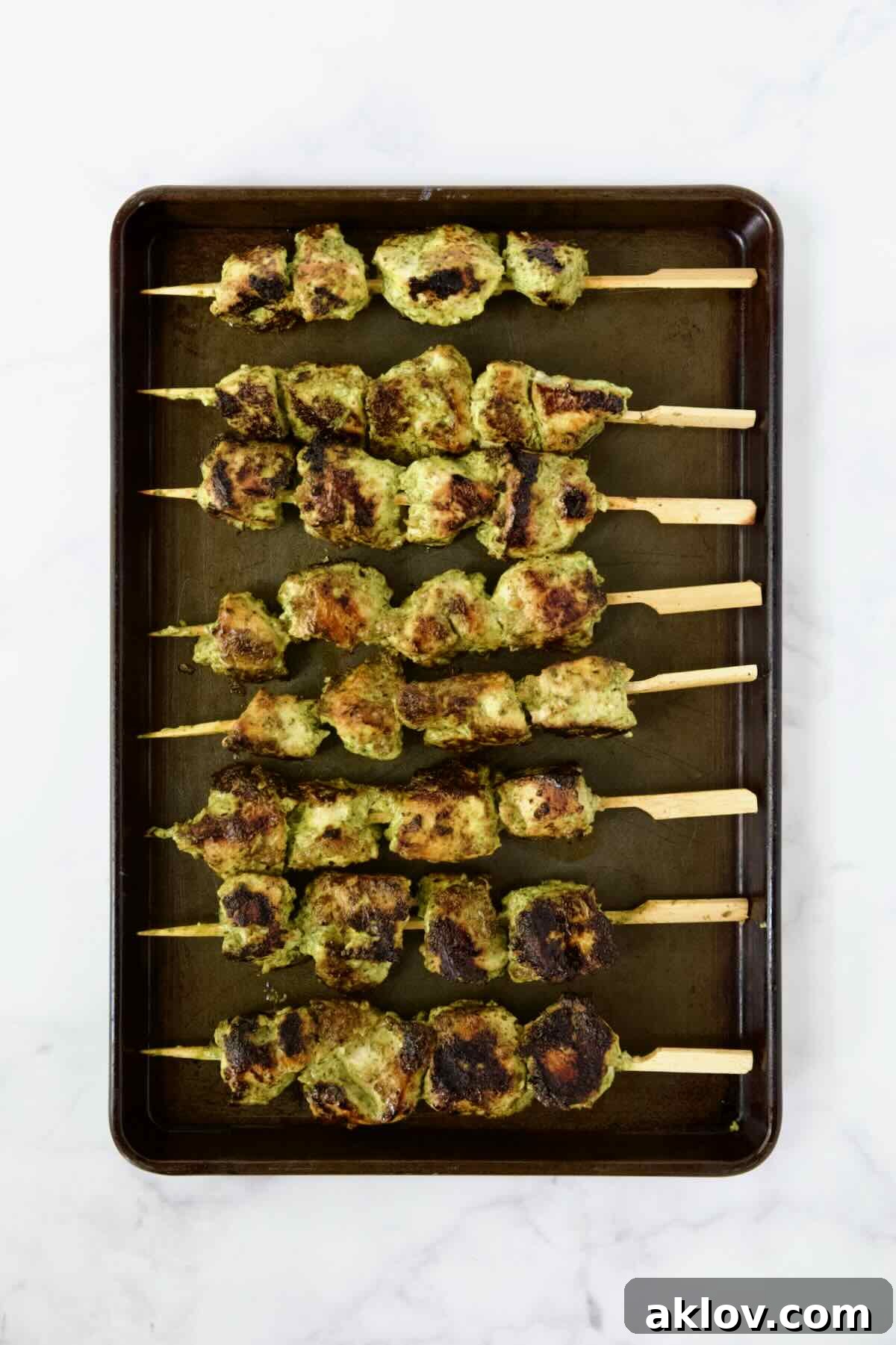 Eight grilled chicken skewers on rimmed sheet pan.