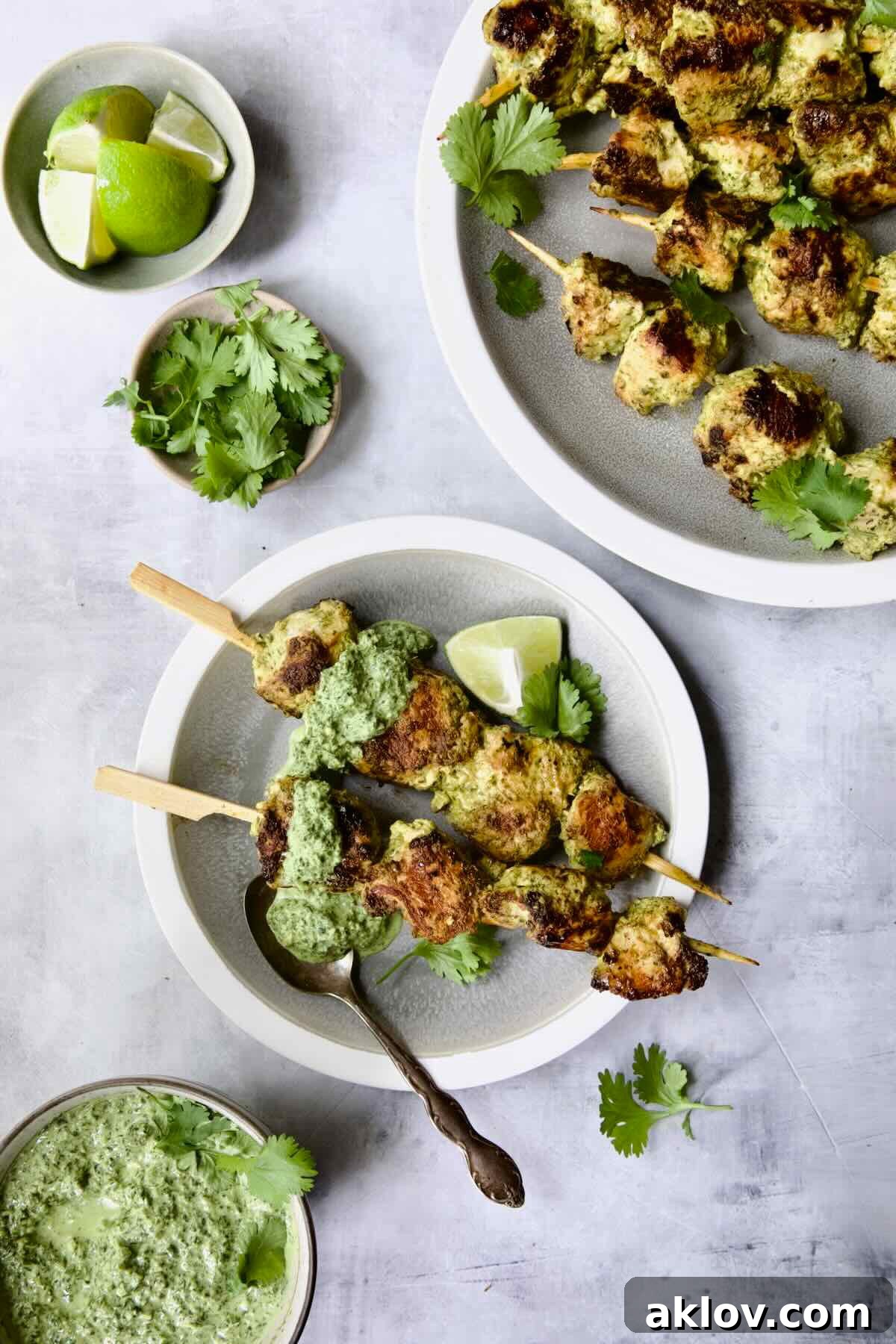 Two Yogurt Marinated Grilled Chicken Skewers with Cilantro Mint Chutney on white and gray plate.