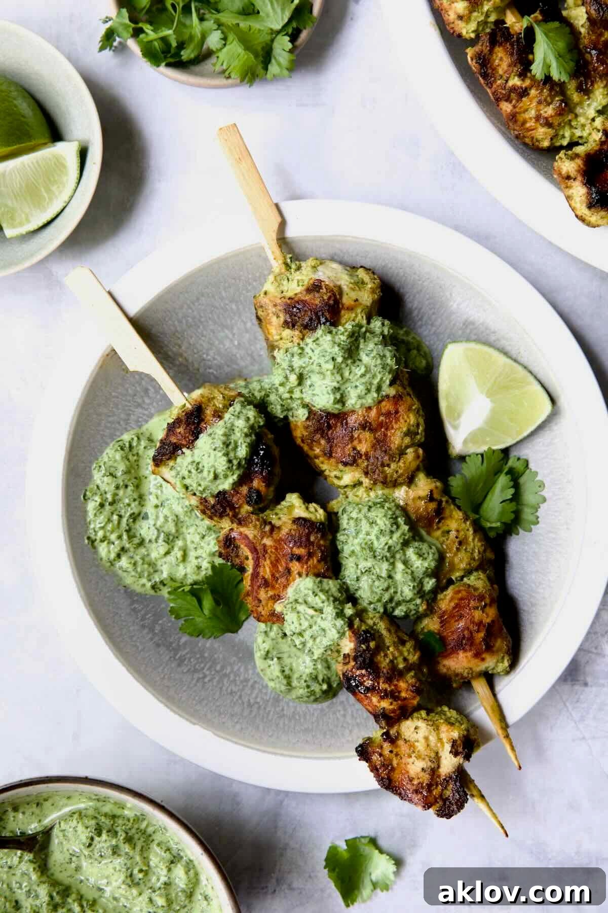 Two Yogurt Marinated Grilled Chicken Skewers with Cilantro Mint Chutney on white and gray plate.