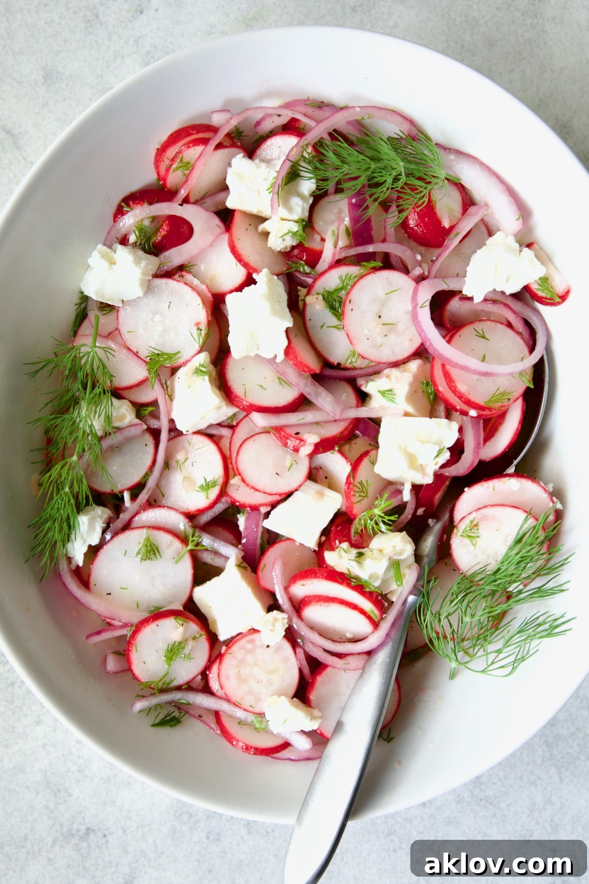 Refreshing Radish Salad 9 Radish Red Onion Salad in white oval serving bowl with serving spoon garnished with fresh dill.