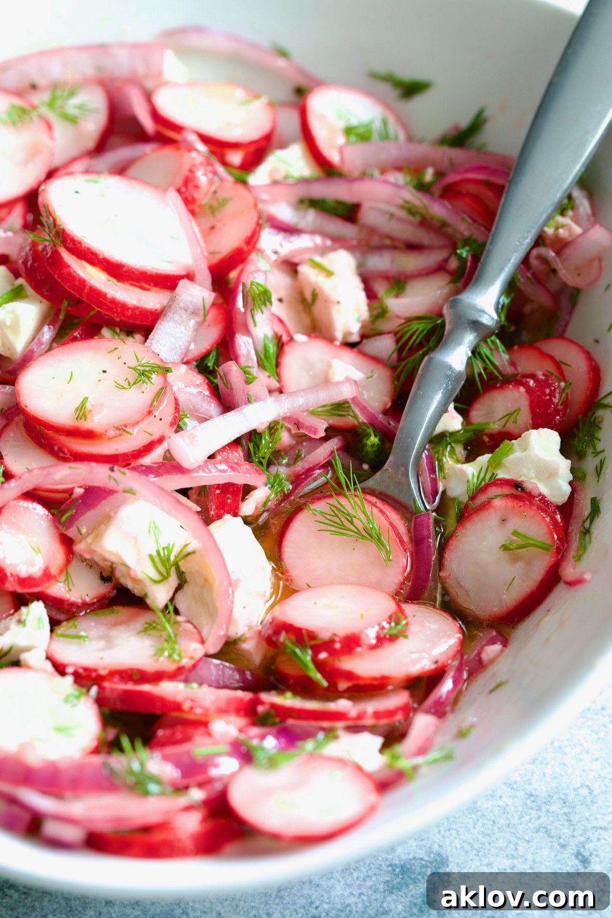 Refreshing Radish Salad 10 Radish Red Onion Salad in white oval serving bowl with serving spoon garnished with fresh dill.