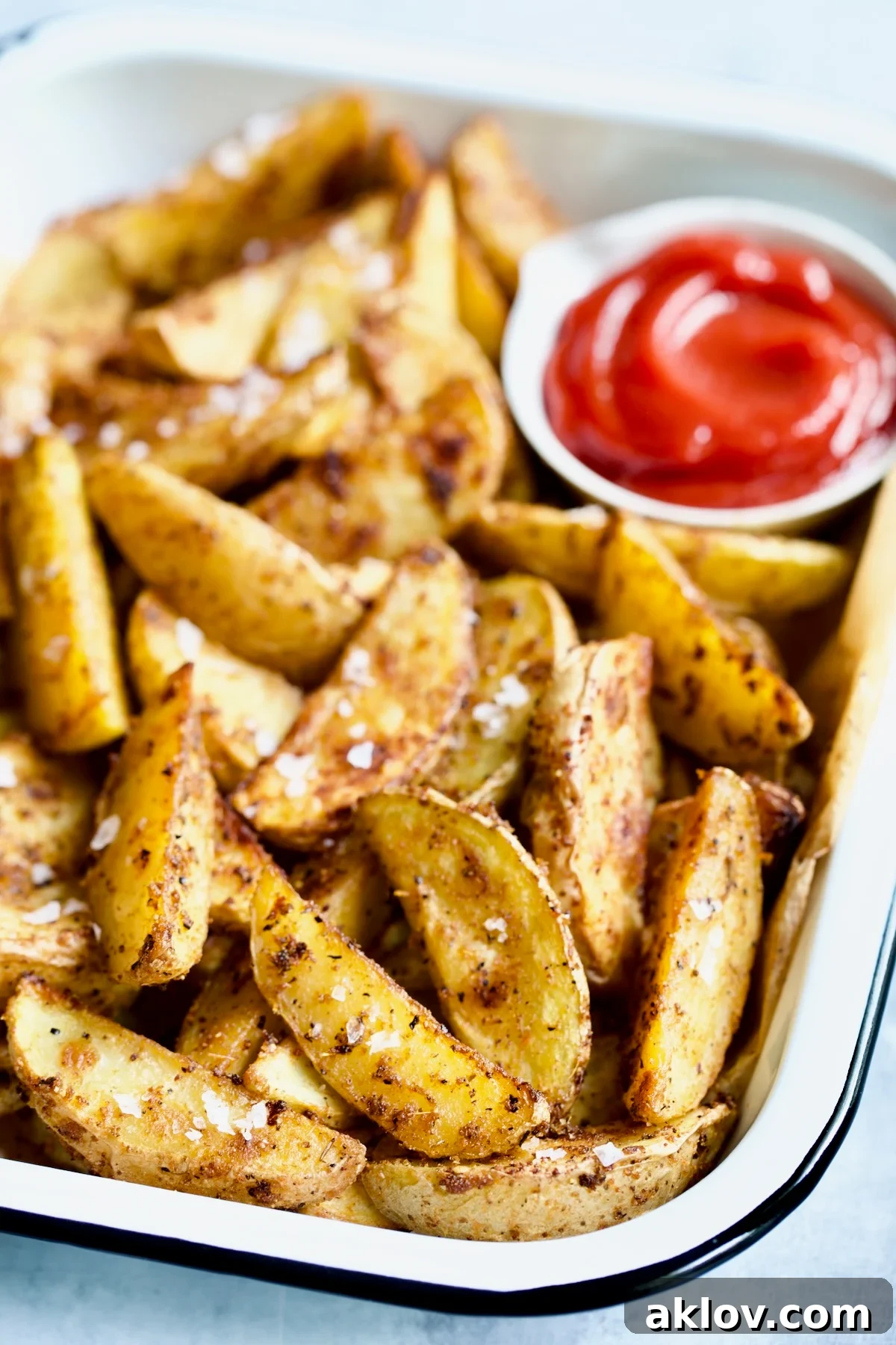 Perfect Roasted Potato Wedges arranged attractively with ketchup in a white enamel tray.