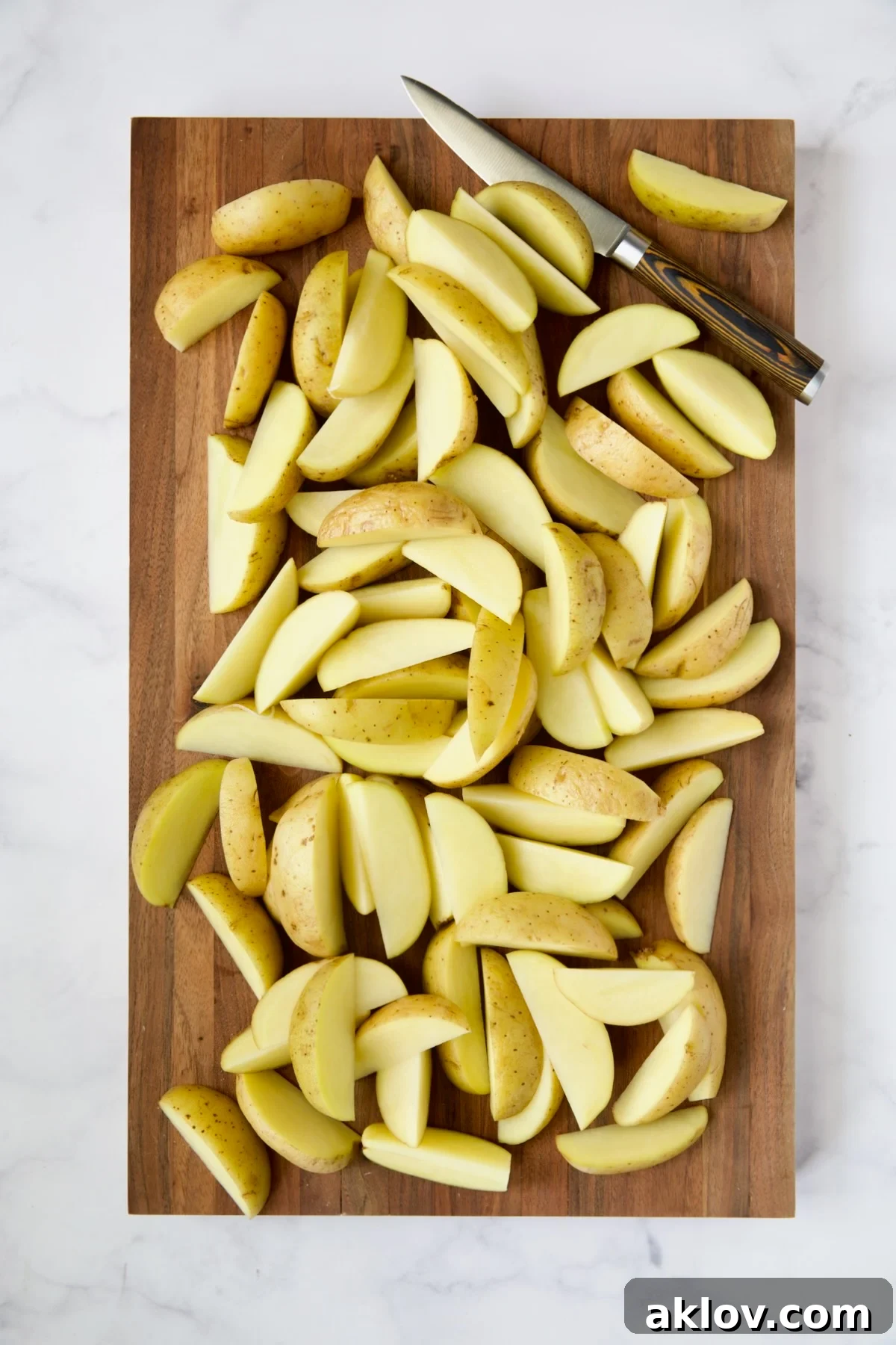Yukon Gold potato wedges expertly cut on a wooden cutting board, alongside a chef's knife.