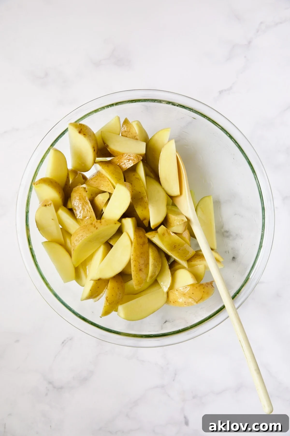 Yukon Gold potato wedges being tossed and coated with olive oil in a glass bowl, ensuring even coverage.