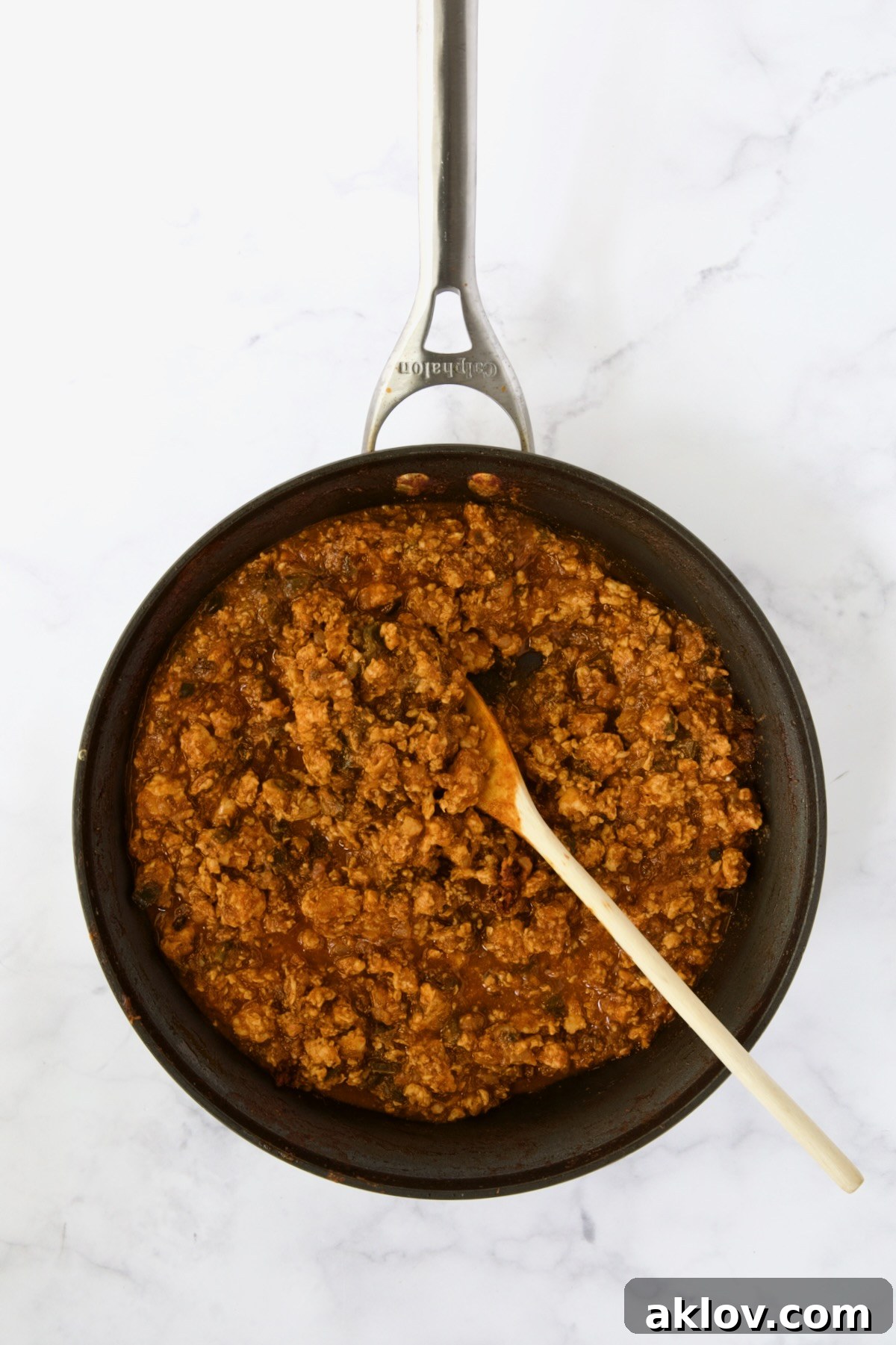 Ground chicken sloppy joes being stirred with wooden spoon in nonstick skillet.