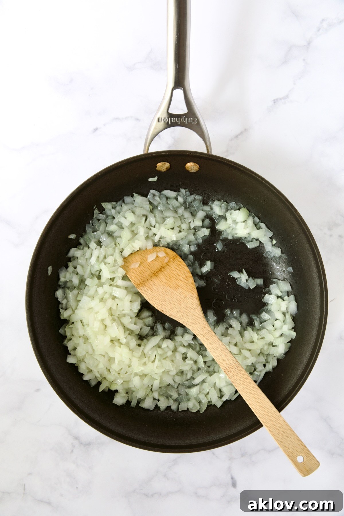Cooked onions in nonstick pan being stirred with wooden spoon.