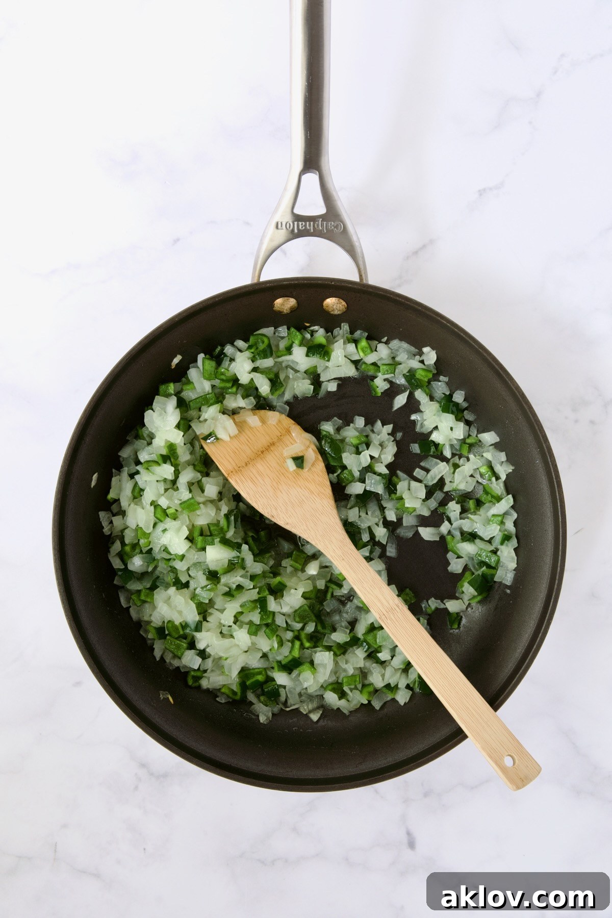Cooked onions and poblano peppers in nonstick skillet being stirred with wooden spoon.