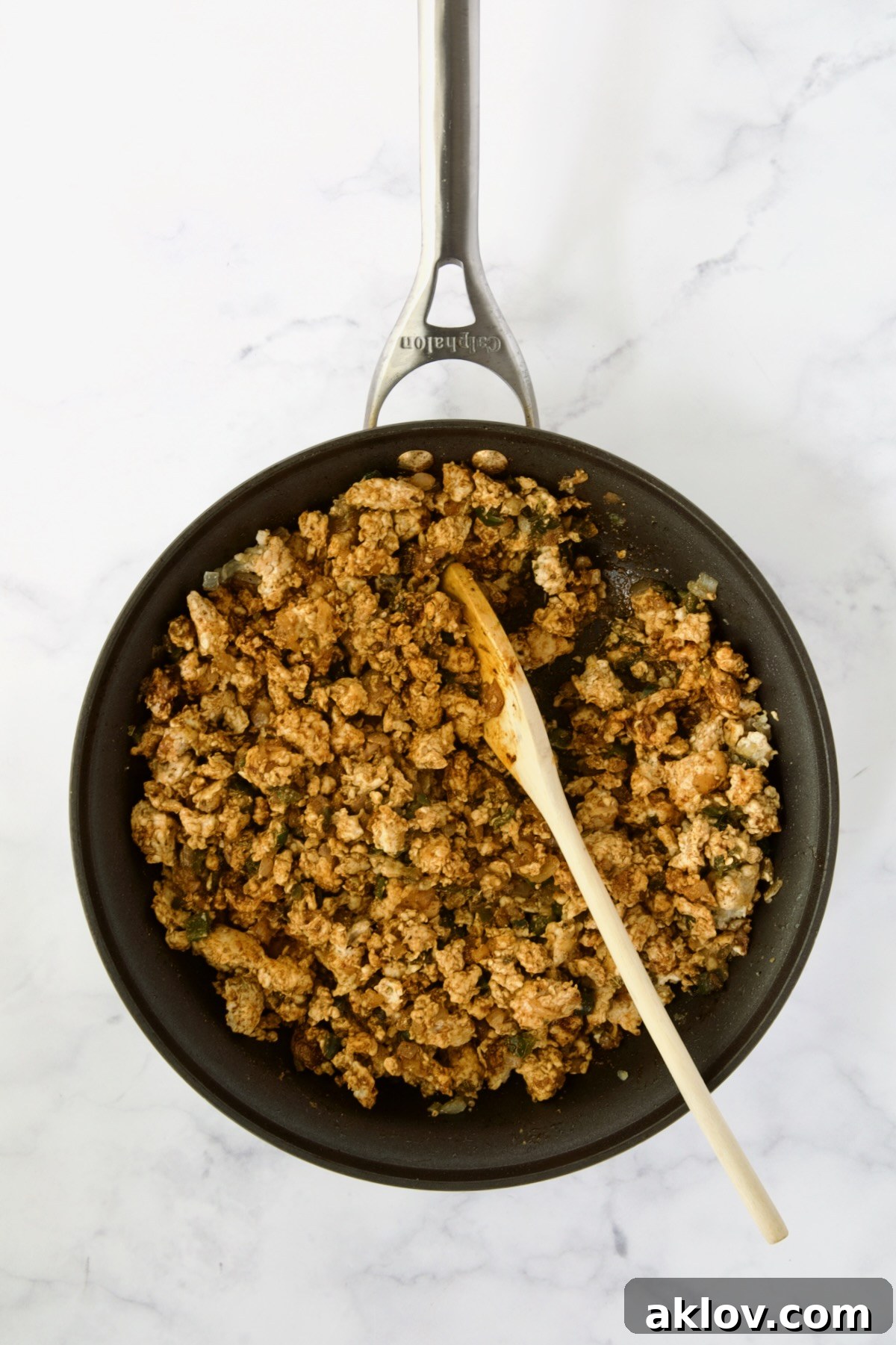 Cooked ground chicken with spices added being stirred with wooden spoon.