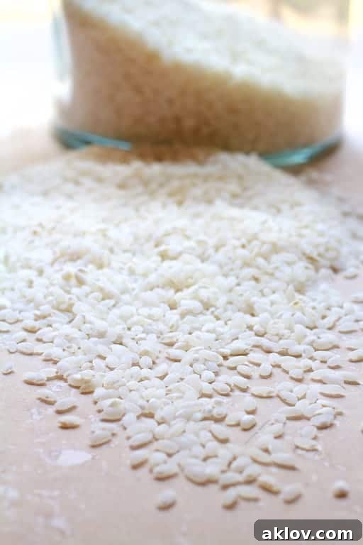 Photo of arborio rice spilled out onto marble surface with jar in the background.