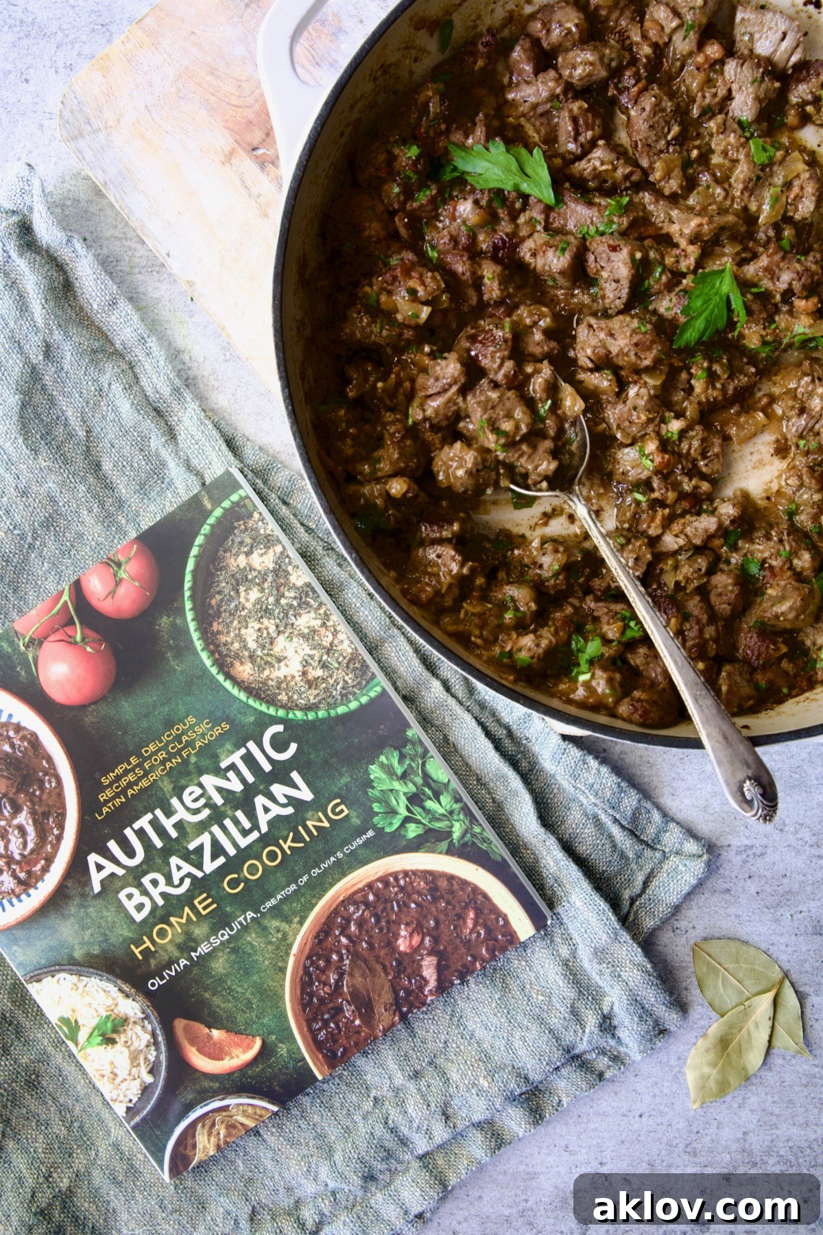 The Authentic Brazilian Home Cooking cookbook displayed alongside a skillet of delicious Beef Tips in Beer Sauce, showcasing the inspiration behind the dish.