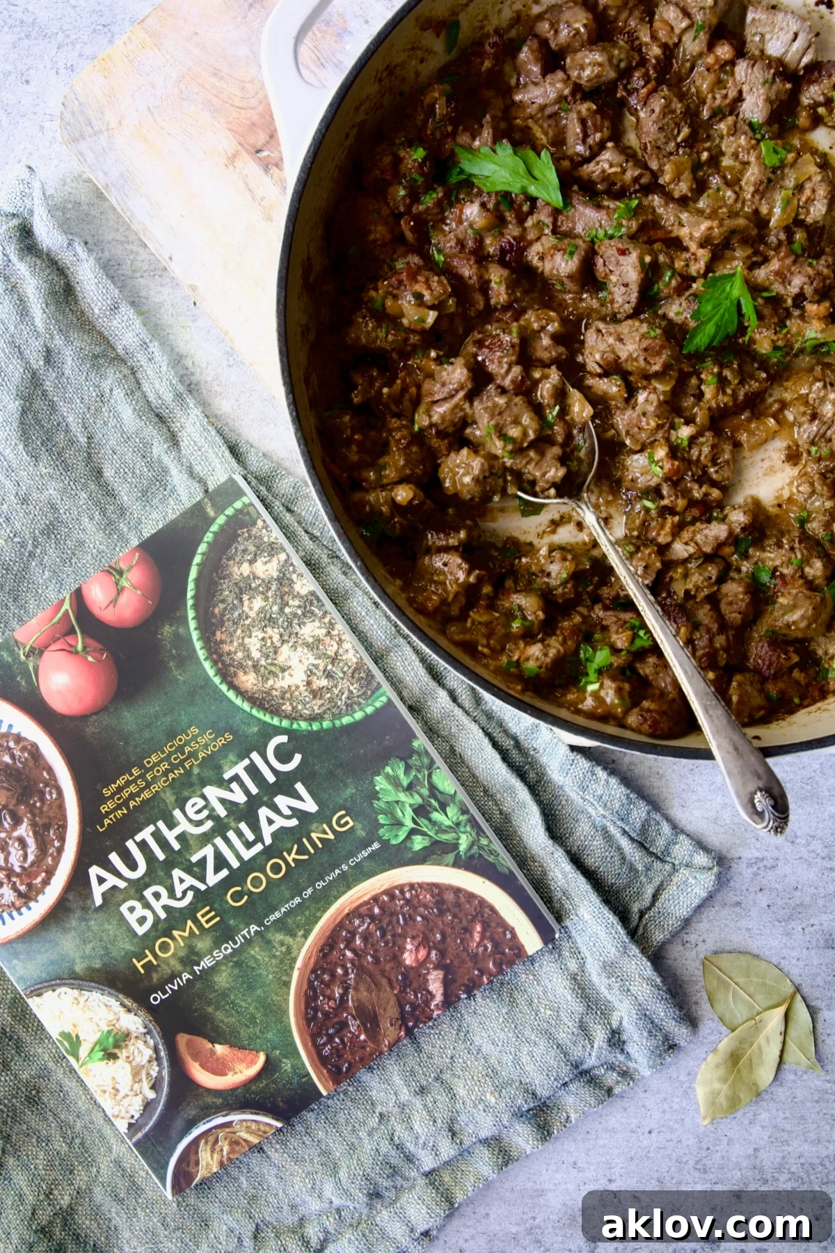 Hearty Beer Braised Beef Tips 4 Olivia Mesquita's 'Authentic Brazilian Home Cooking' cookbook displayed alongside a skillet of Beef Tips in Beer Sauce, highlighting the connection between the recipe and its source.