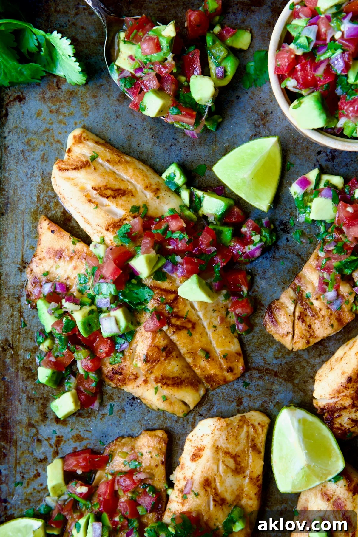 Grilled Tilapia with Tomato - Avocado Salsa with lime wedges on a sheet pan, ready to serve.