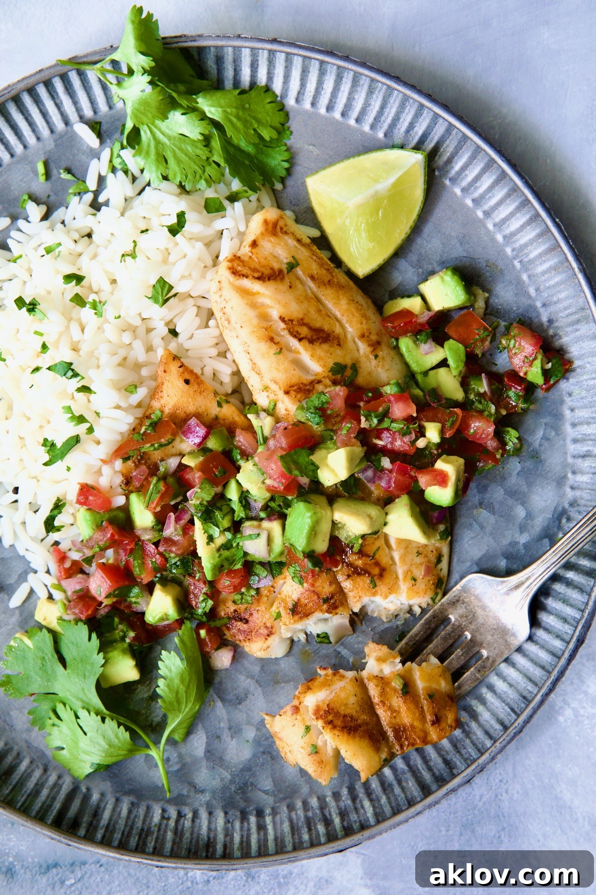 Grilled Tilapia with Tomato - Avocado Salsa on a round metal plate with a fork ready to eat a piece.