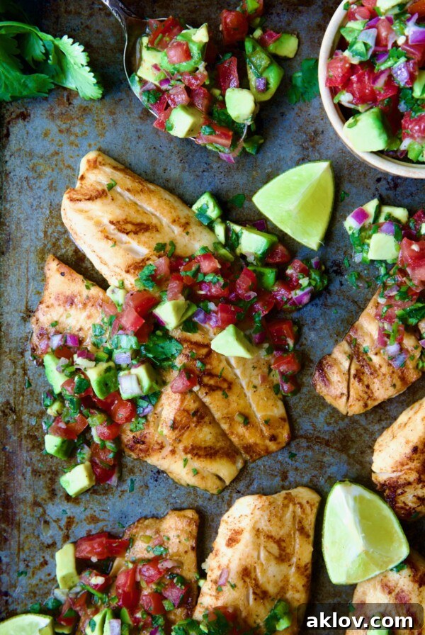 Grilled Tilapia with Tomato - Avocado Salsa with lime wedges on a sheet pan.