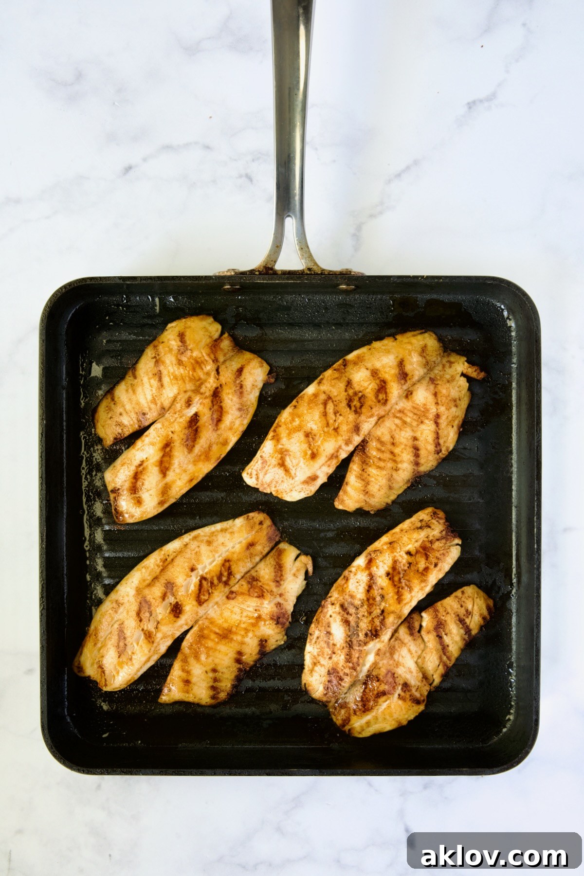 Four pieces of grilled tilapia cooking on a nonstick square grill pan.