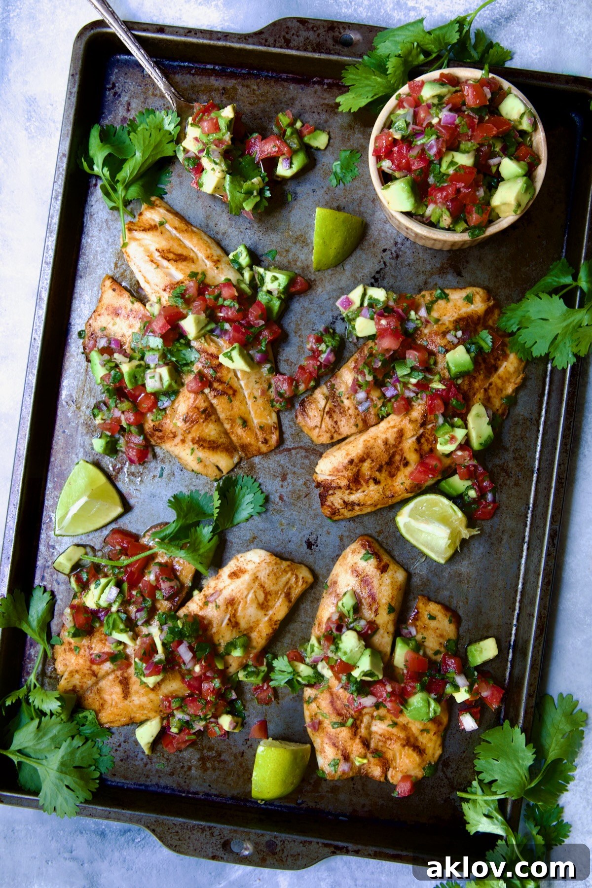 Four pieces of Grilled Tilapia with Tomato - Avocado Salsa beautifully plated on a sheet pan.