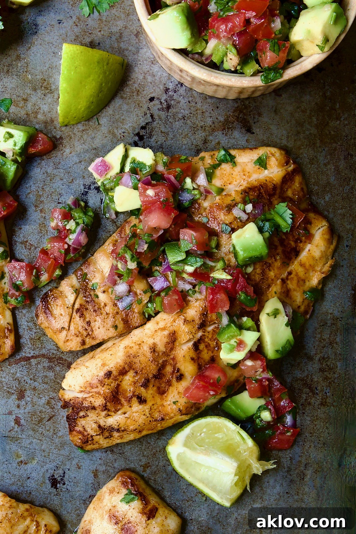 One piece of Grilled Tilapia with Tomato - Avocado Salsa, garnished with a lime wedge and cilantro.