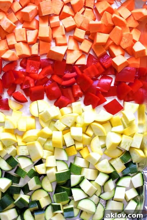 Uncooked sweet potatoes, red peppers, zucchini, and yellow squash arranged on a baking sheet, ready for roasting.