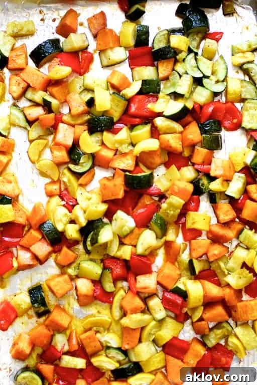 Perfectly roasted sweet potatoes, red peppers, zucchini, and yellow squash glistening on a baking sheet after being cooked.