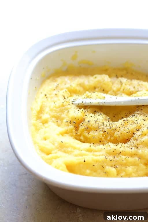 Creamy polenta being stirred in a white baking dish with a white spoon, showcasing its smooth texture.