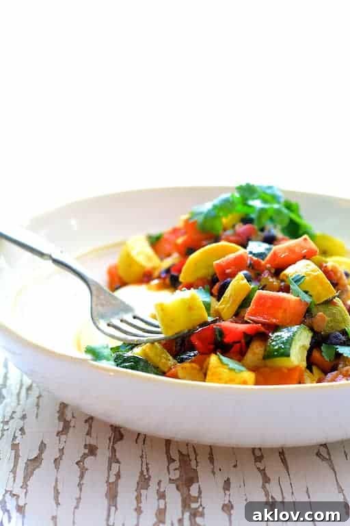A close-up shot of Spicy Roasted Vegetable and Black Bean Stew with Polenta in a white bowl, with a fork lifting a delicious bite.