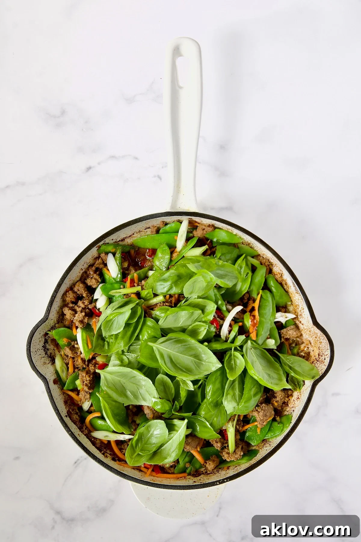 Spicy Thai Basil Beef Stir-fry 12 The final step: cooked ground beef, vegetables, and scallions are now mixed with a generous amount of fresh basil leaves, which are just beginning to wilt from the residual heat.