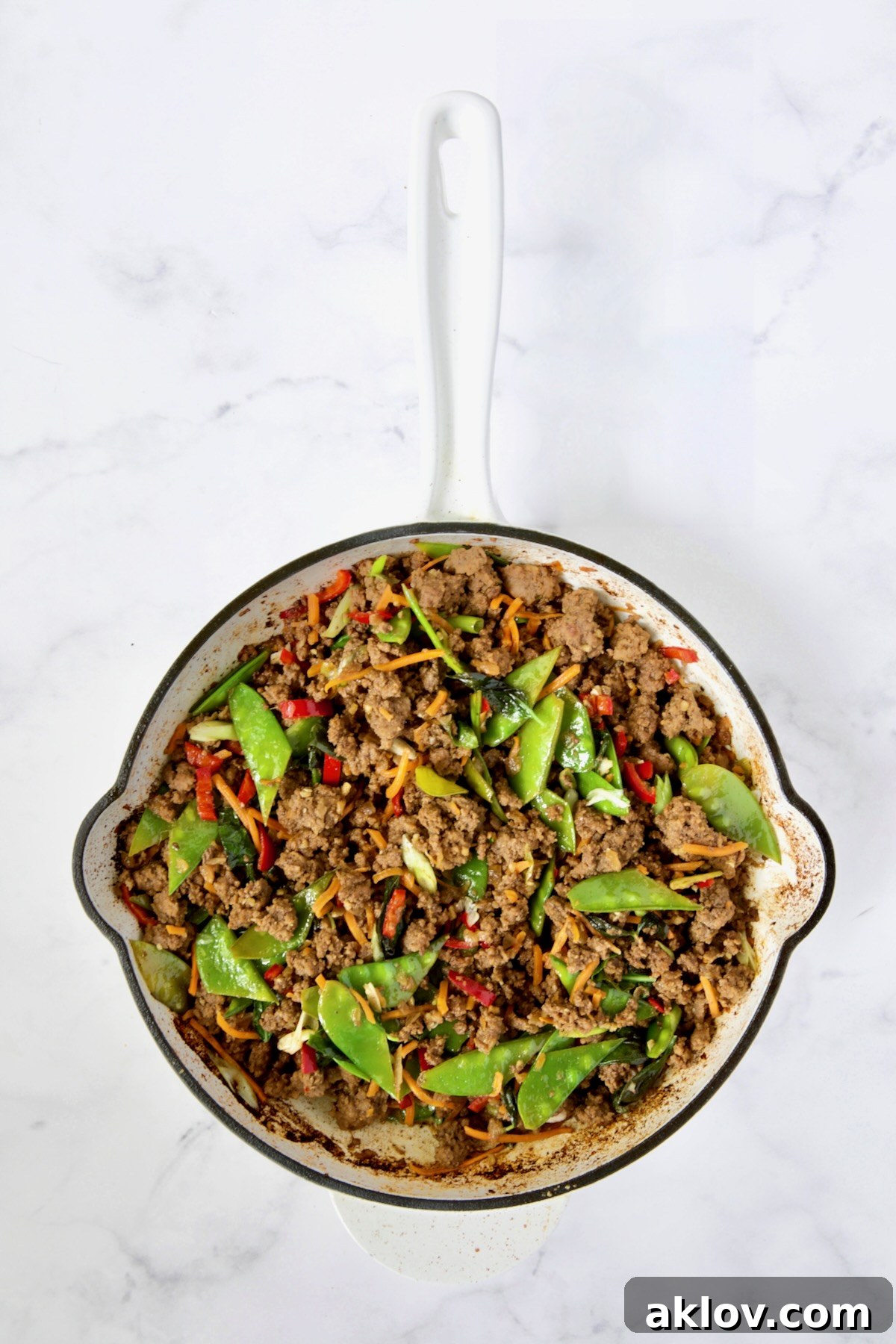 A final shot of the Thai Basil Beef stir-fry nestled in a white enamel cast iron skillet, ready to be served, highlighting its rich textures and inviting colors.