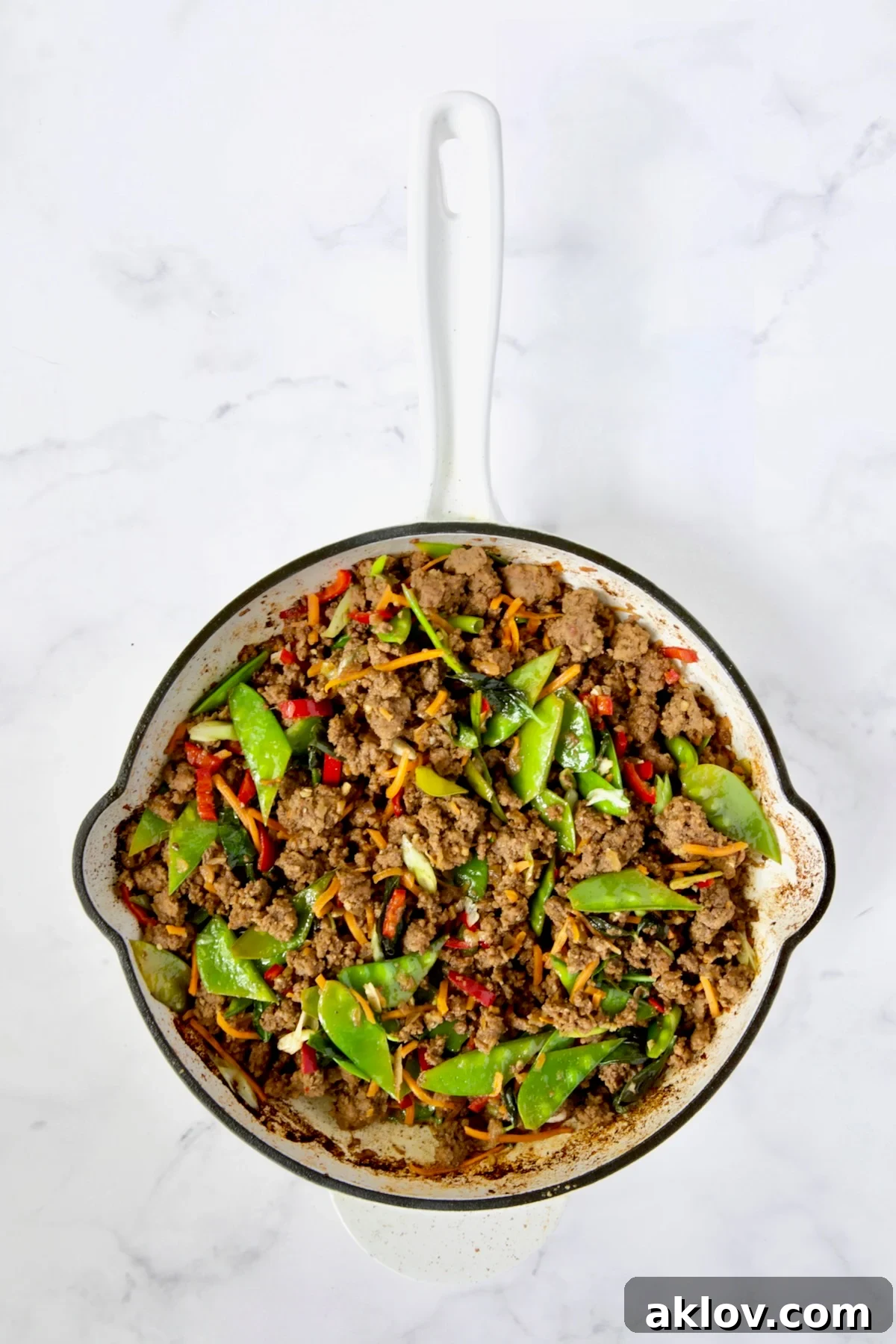 Spicy Thai Basil Beef Stir-fry 13 The finished Thai Basil Beef stir-fry rests in the white enamel cast iron skillet, a harmonious blend of colors and textures, ready for serving.