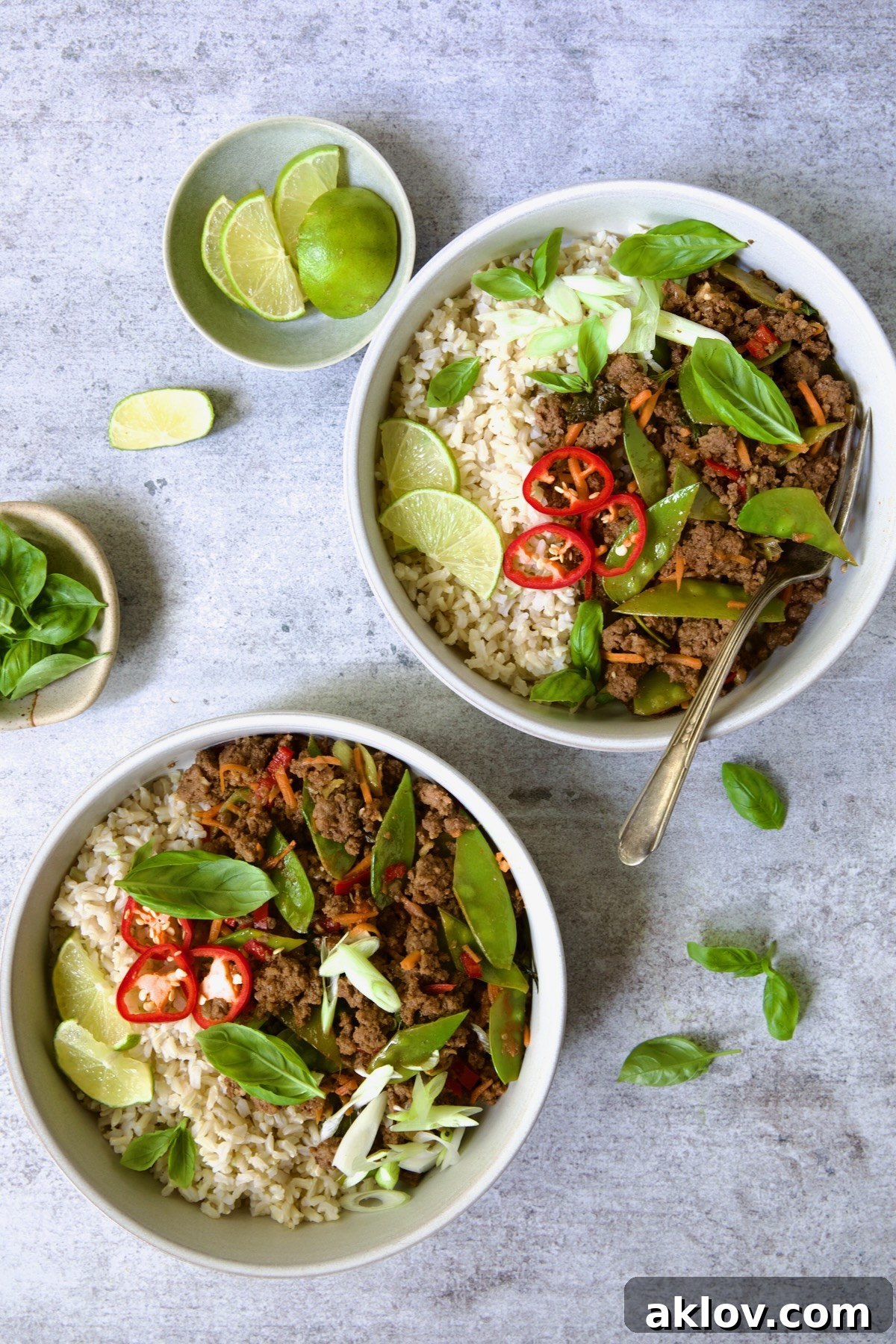 Two bowls of Thai Basil Beef, presented with elegant simplicity, highlighting the rich colors and textures of the stir-fry and its perfect pairing with rice.