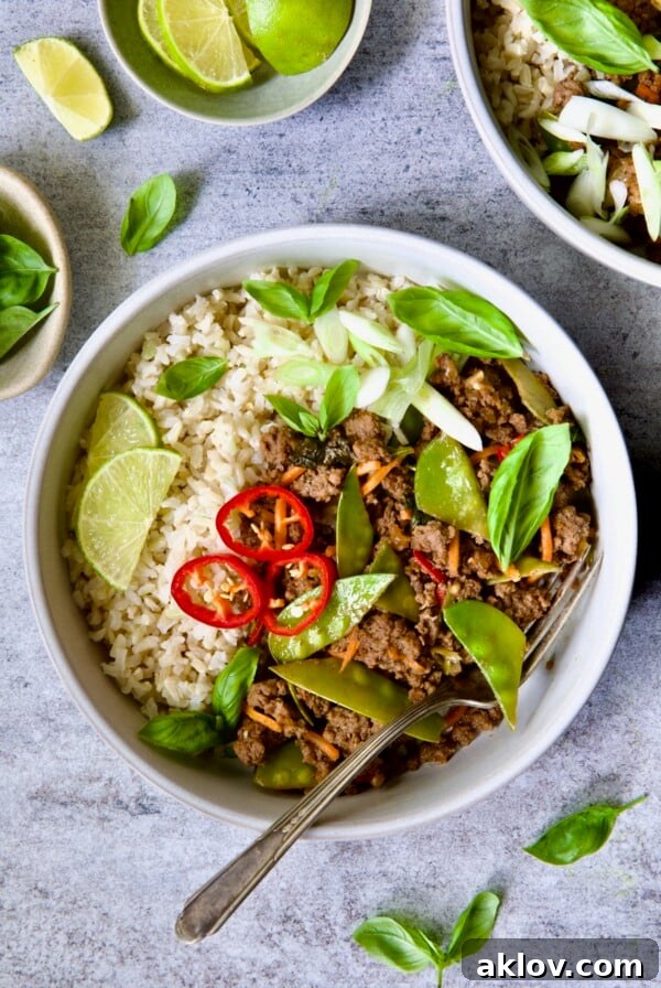 Thai Basil Beef in white bowl garnished with lime wedges, fresh basil and Fresno chiles.