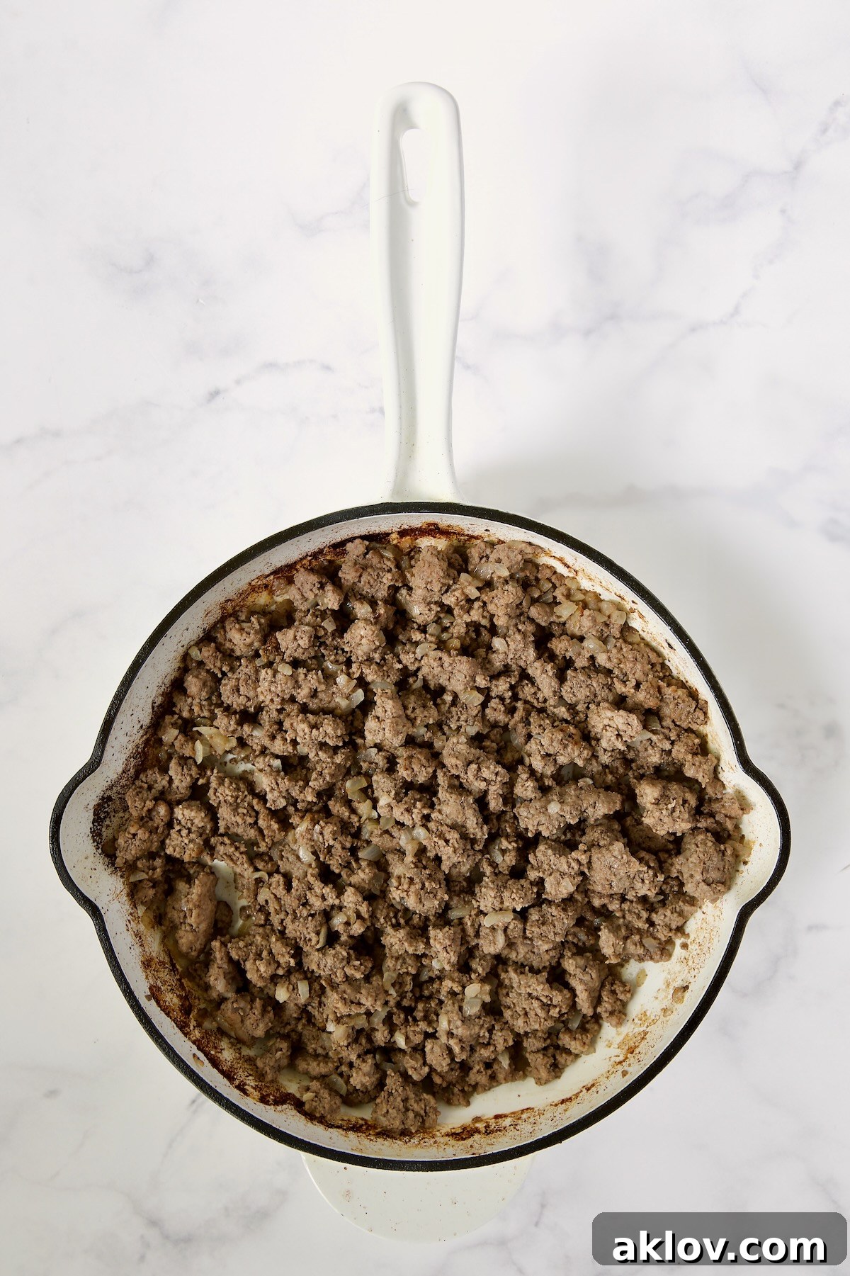 The ground beef is perfectly browned and crumbled in a white enamel cast iron skillet, showcasing its rich texture and readiness for the next steps in the stir-fry process.