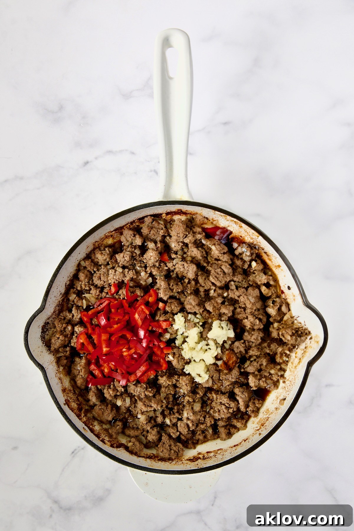 Cooked ground beef with Fresno chiles and garlic just added to a white enamel cast iron skillet, filling the air with enticing aromas.