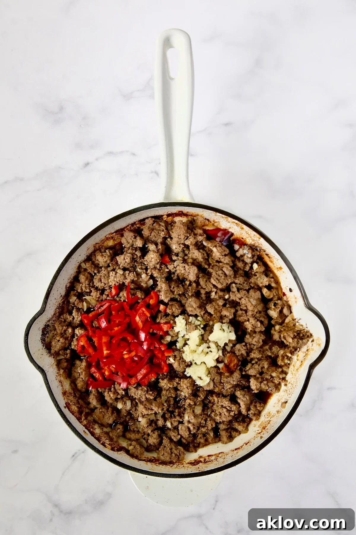 Spicy Thai Basil Beef Stir-fry 8 Cooked ground beef in a white enamel cast iron skillet, with aromatic Fresno chiles and minced garlic freshly added, beginning to infuse their flavors.