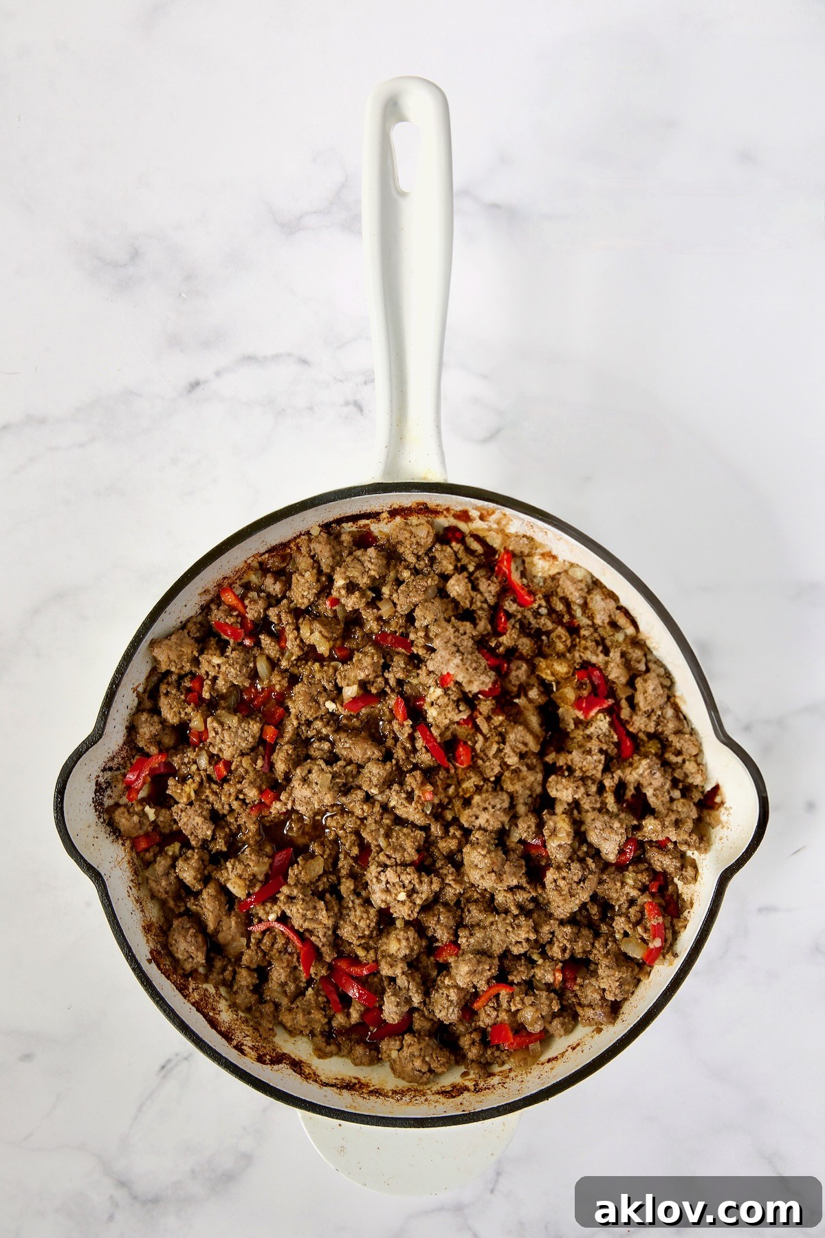 Cooked ground beef and Fresno chiles are shown together in a white enamel cast iron skillet, after the garlic has been incorporated, creating a flavorful base.
