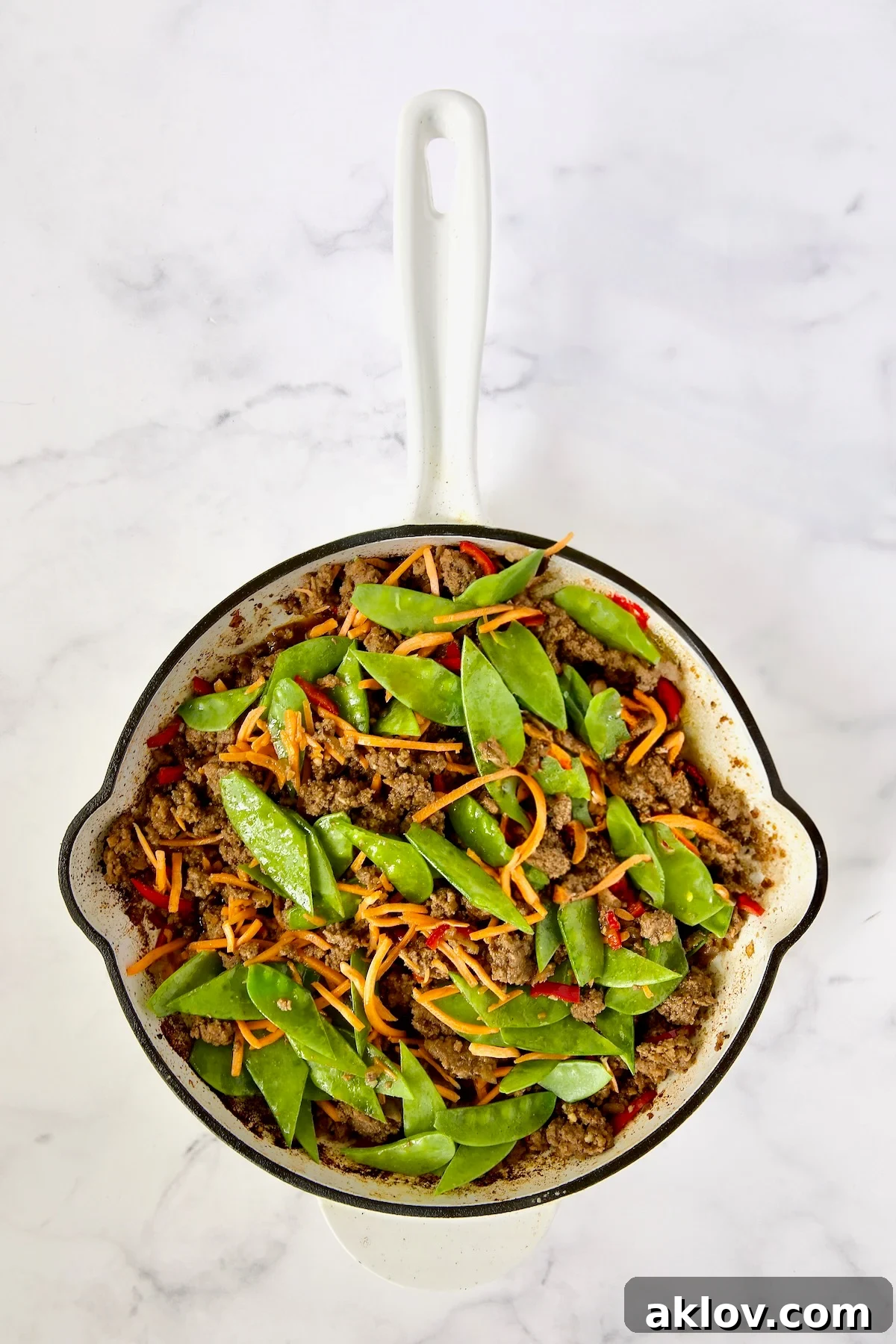 Spicy Thai Basil Beef Stir-fry 10 The skillet now holds cooked ground beef, Fresno chiles, and freshly added shredded carrots and snow peas, coated in the simmering sauce.
