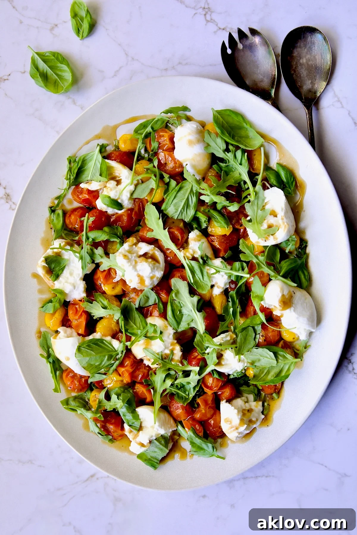 Creamy Burrata Caprese with Sweet Roasted Cherry Tomatoes 2 Roasted Cherry Tomato Burrata Caprese Salad on white oval platter with serving utensils.