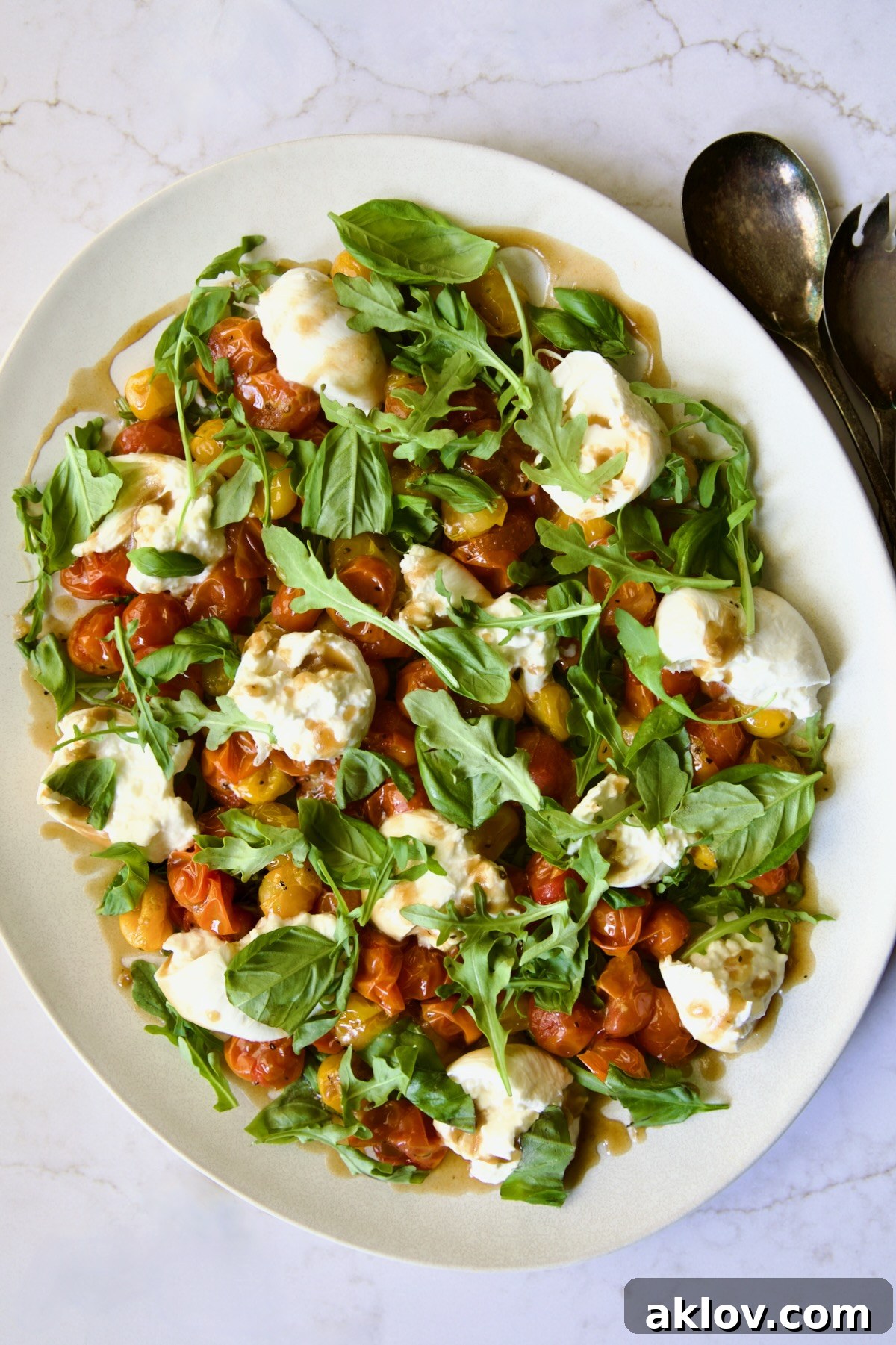 Creamy Burrata Caprese with Sweet Roasted Cherry Tomatoes 13 Roasted Cherry Tomato Burrata Caprese Salad on white oval platter with serving utensils, ready to be served.