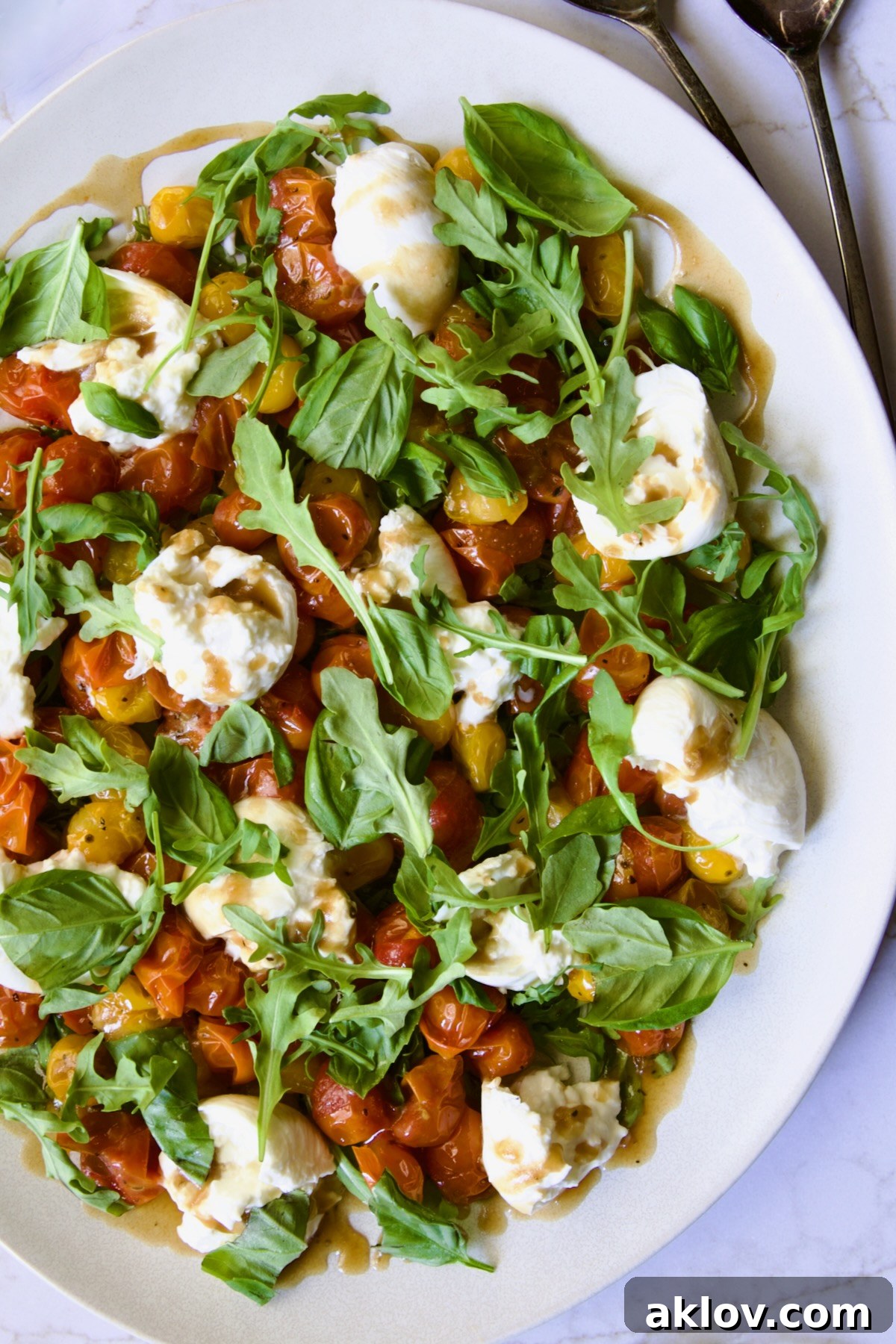 Creamy Burrata Caprese with Sweet Roasted Cherry Tomatoes 15 Roasted Cherry Tomato Burrata Caprese Salad on white oval platter with serving utensils, ready for enjoyment.