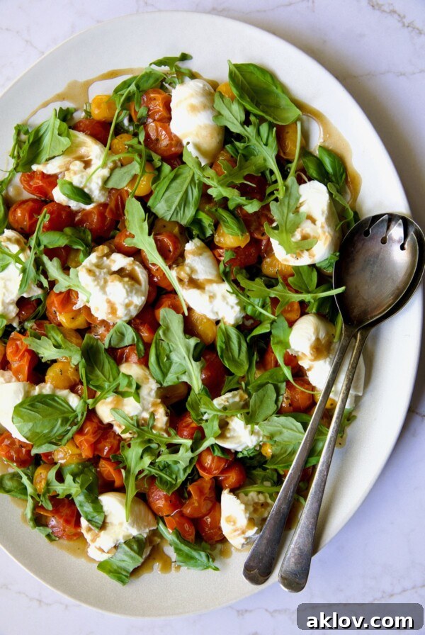 Roasted Cherry Tomato Burrata Caprese Salad on white oval platter with serving utensils.
