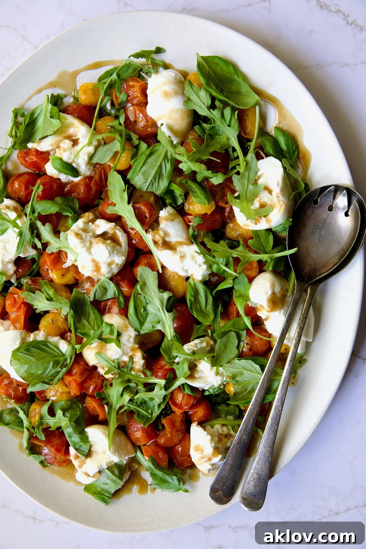 Creamy Burrata Caprese with Sweet Roasted Cherry Tomatoes 3 Roasted Cherry Tomato Burrata Caprese Salad on white oval platter with serving utensils.