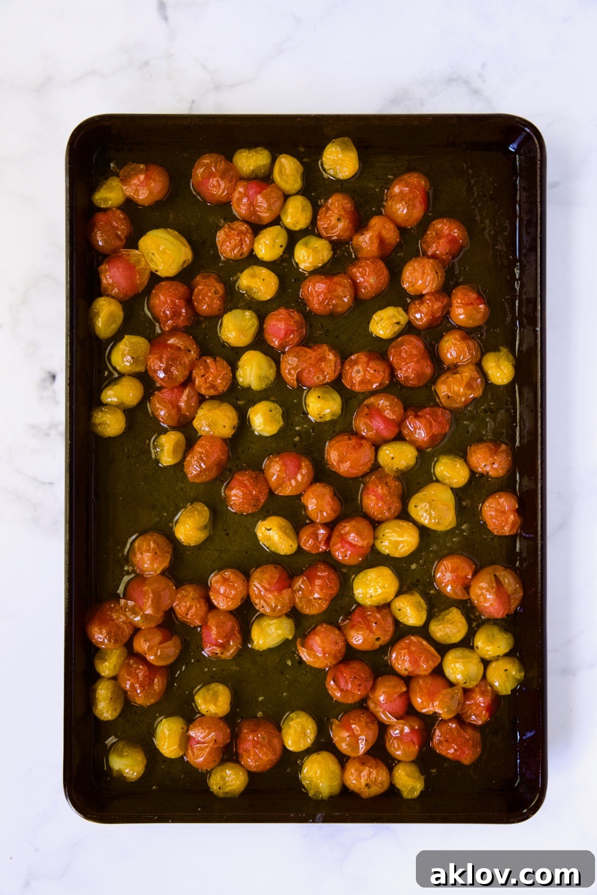 Creamy Burrata Caprese with Sweet Roasted Cherry Tomatoes 7 Red and yellow cherry tomatoes on a rimmed baking sheet after being roasted, showing their softened, slightly burst appearance and released juices.