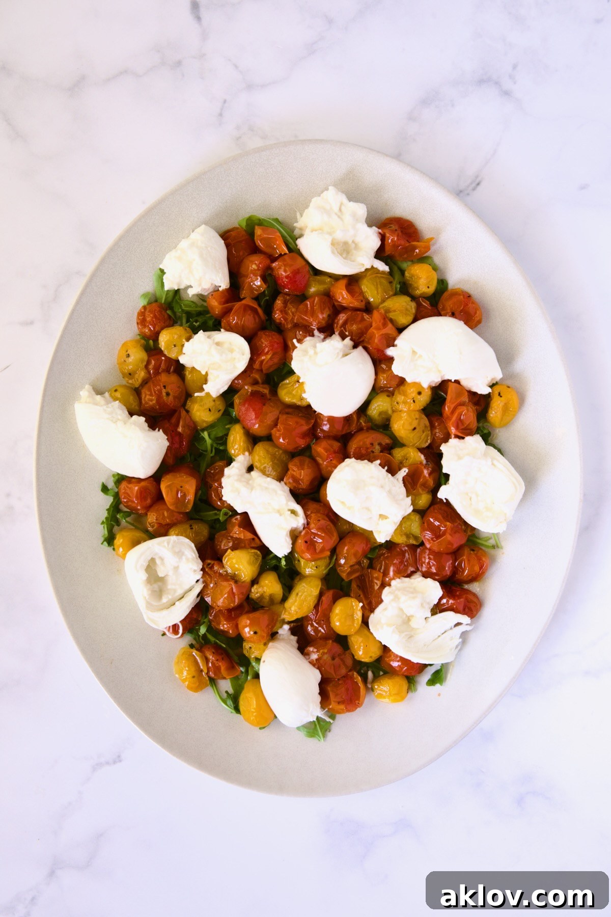 Creamy Burrata Caprese with Sweet Roasted Cherry Tomatoes 10 Creamy burrata pieces and roasted cherry tomatoes artfully arranged on a bed of arugula on a white oval platter.