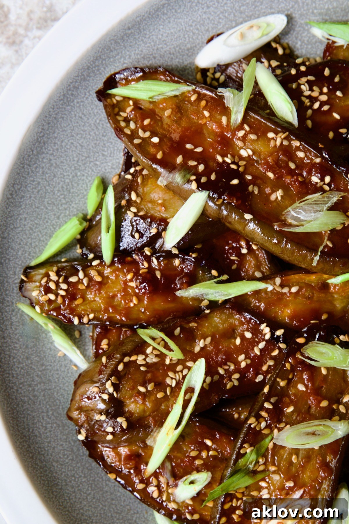 Gochujang Eggplant on round gray plate with white rim garnished with scallions and sesame seeds.