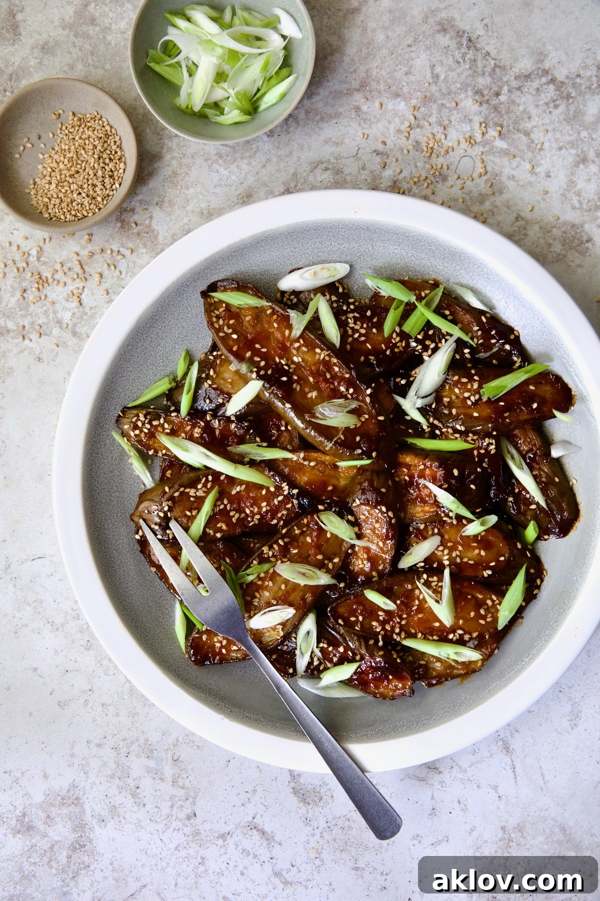 Gochujang Eggplant on round gray plate with white rim garnished with scallions and sesame seeds.