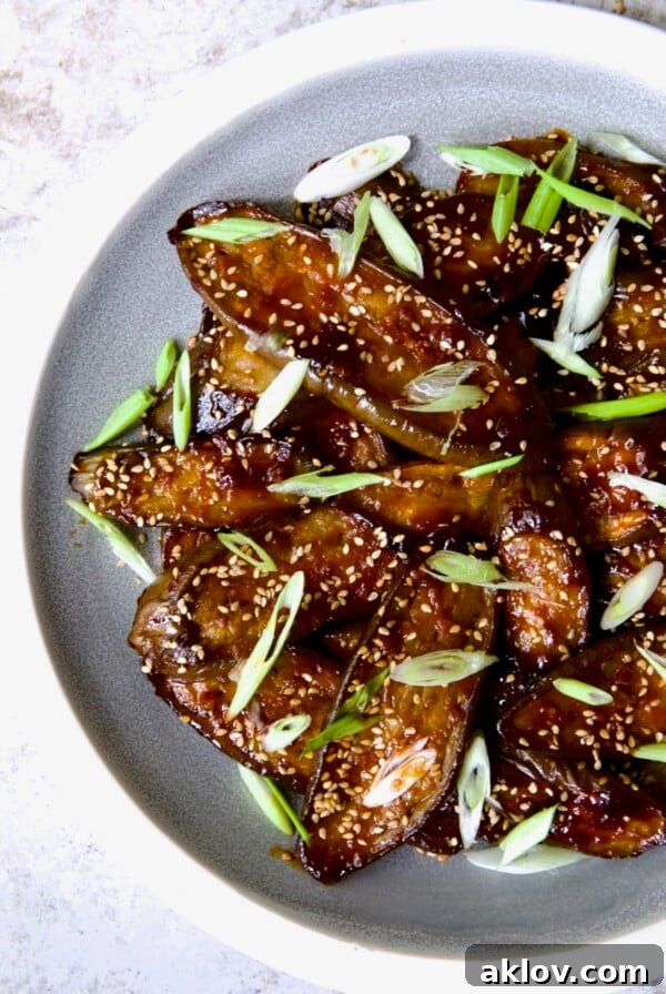 Gochujang Eggplant on round gray plate with white rim garnished with scallions and sesame seeds.
