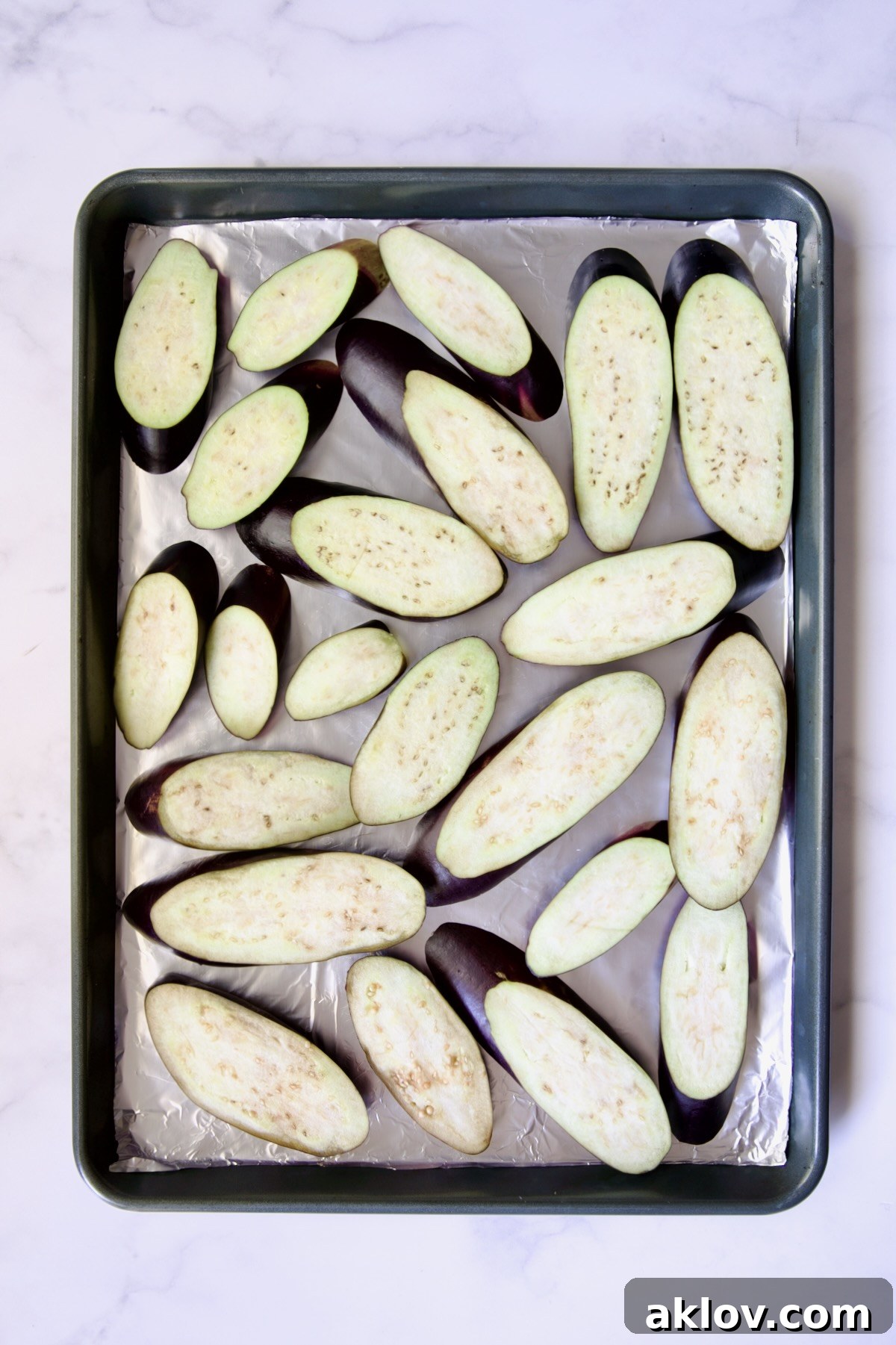 Slices of eggplant cut on the diagonal on aluminum foil-lined rimmed sheet pan.
