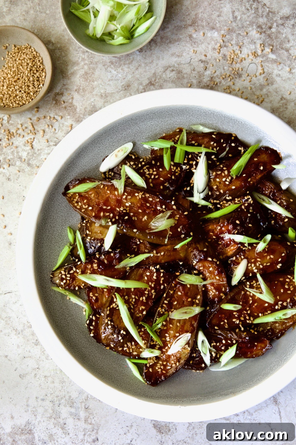 Gochujang Eggplant on round gray plate with white rim garnished with scallions and sesame seeds.