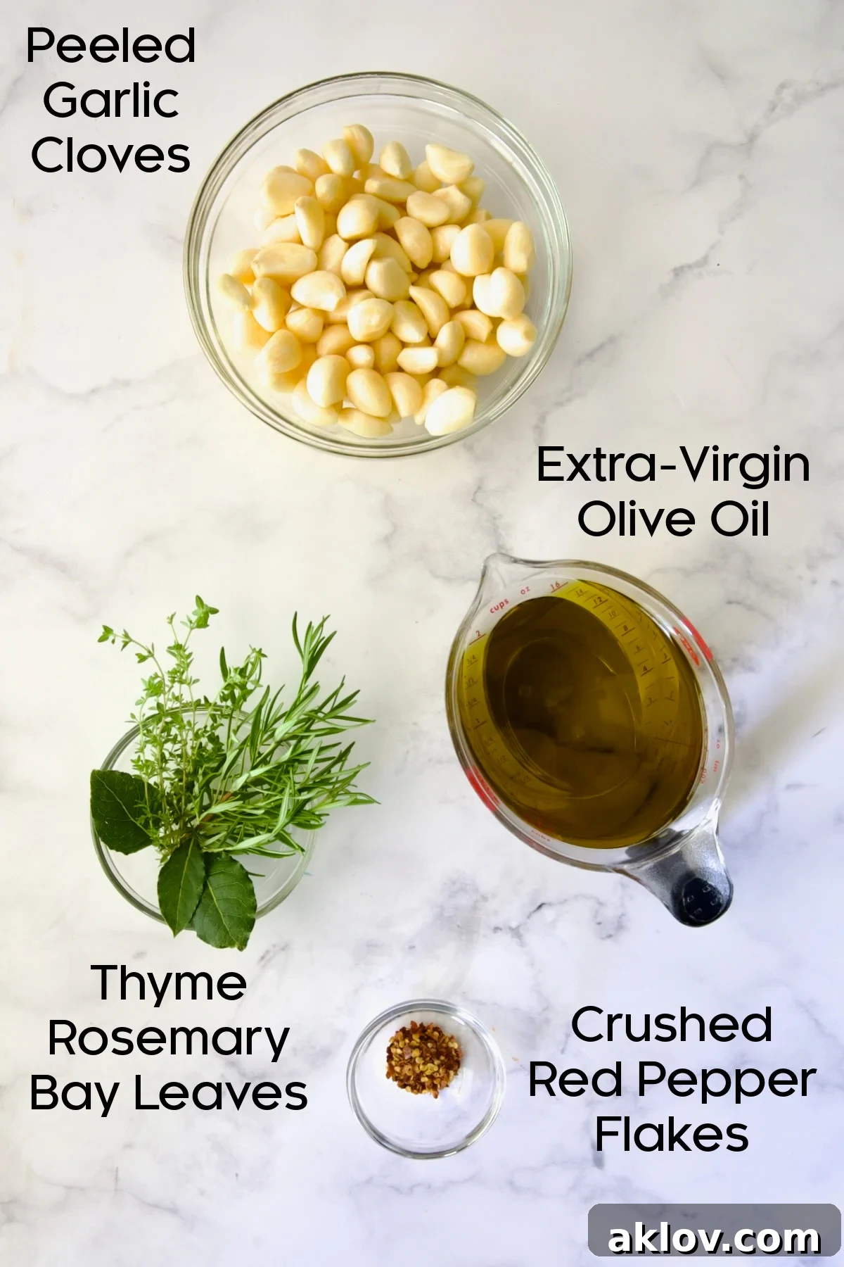 All the fresh ingredients for garlic confit, including peeled garlic cloves, fresh herbs, and red pepper flakes.