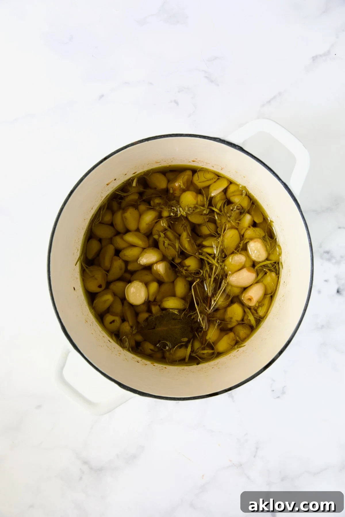 Cooked garlic confit in a white Dutch oven, golden and tender after simmering in olive oil with herbs.